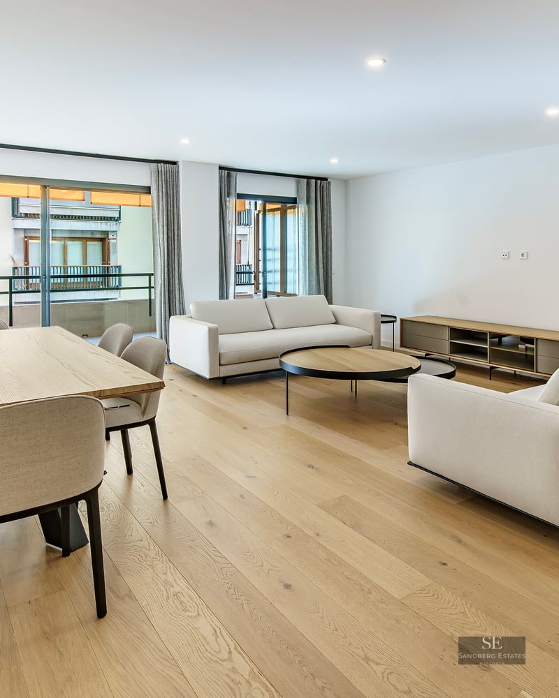 Séjour ouvert avec canapés blancs, table à manger en bois et grandes baies vitrées donnant sur un balcon.