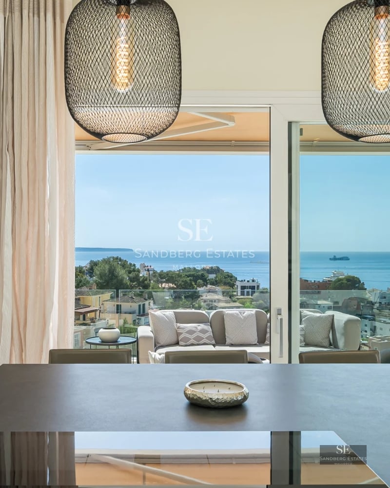 Exterior of a modern villa with a pool, lush greenery, and a large window reflecting sunlight.