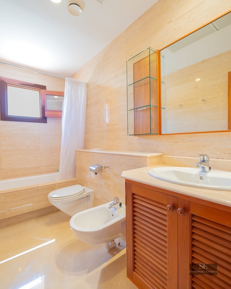 Bathroom featuring beige marble walls, a bathtub, bidet, toilet, and wooden vanity unit.