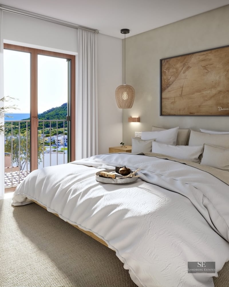 Bright modern bedroom with white bed, wicker lamps, wooden nightstands, and a balcony overlooking the sea and mountains.