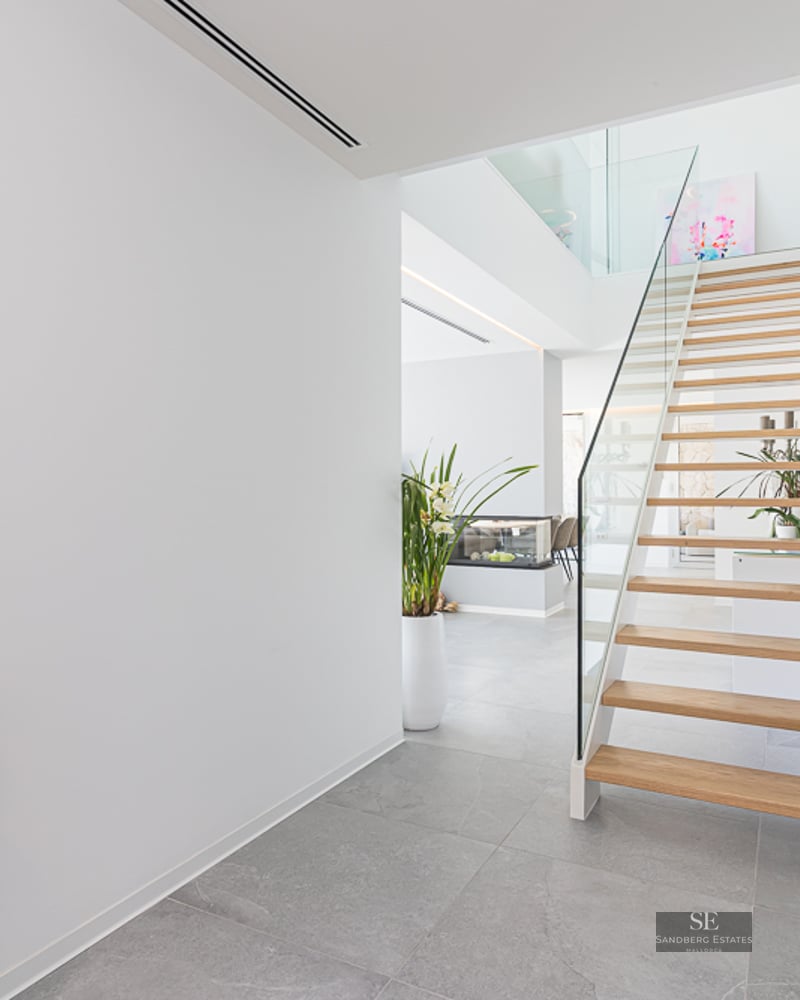 Bright modern hallway featuring a light wood floating staircase with glass railings and grey stone flooring.