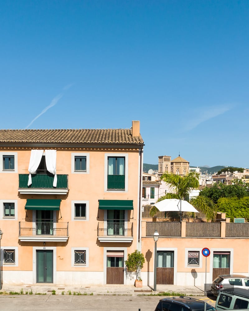 Three-story terracotta building with green balconies and awnings under a clear blue sky.
