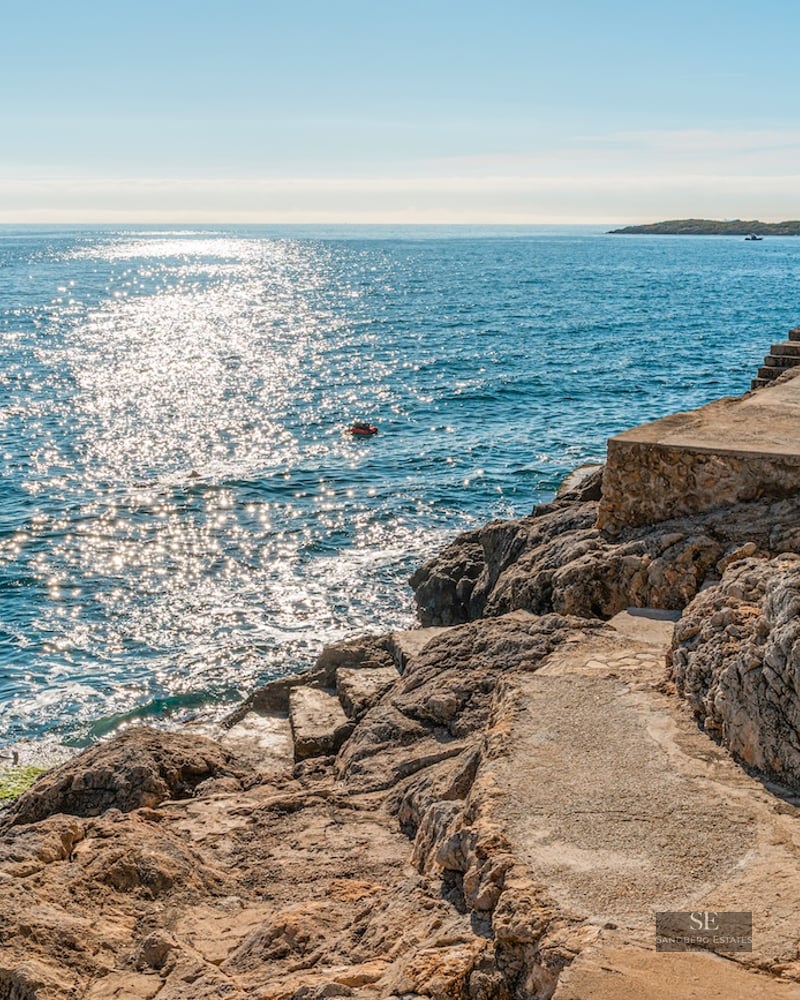 Stone terrace on a rocky coastline overlooking sparkling blue sea under bright sunlight.