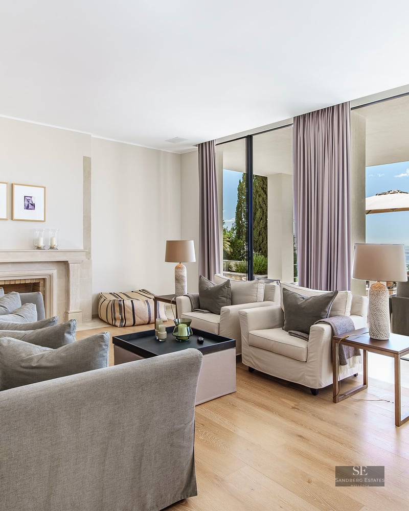 Modern living room with grey sofas, a stone fireplace, and floor-to-ceiling windows opening to a sea-view terrace.