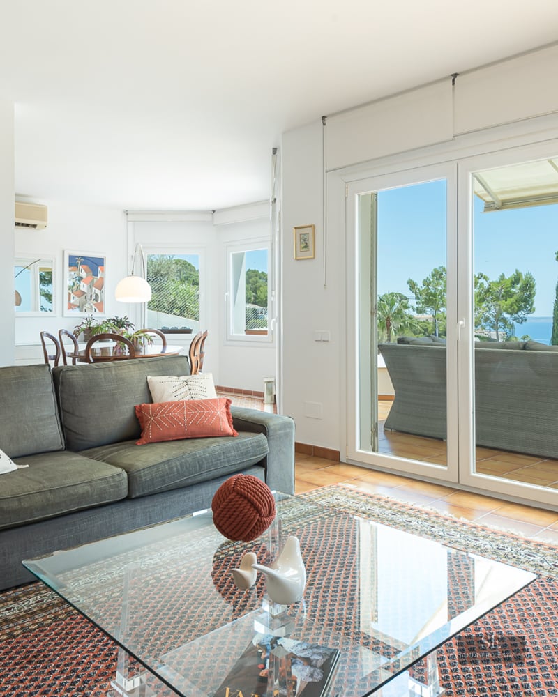 Spacious living room with green sofa, oriental rug, and glass doors opening to a terrace with sea views.