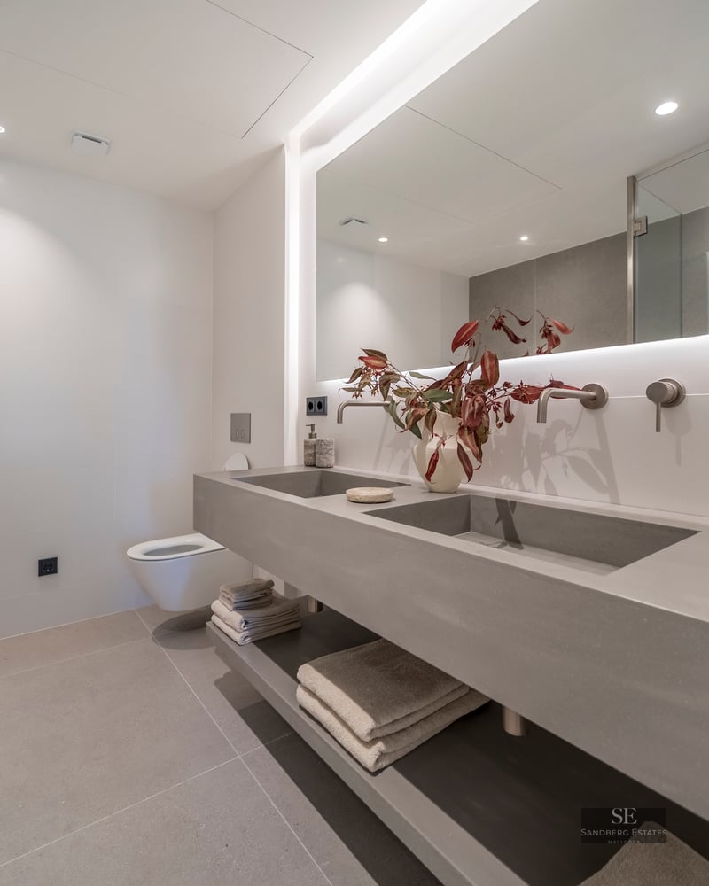 Minimalist bathroom featuring a floating grey concrete double vanity, large backlit mirror, and wall-mounted faucets.