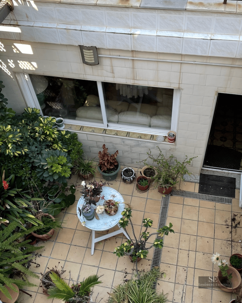 Overhead view of a tiled patio with a metal staircase, numerous potted plants, and a small white round table.