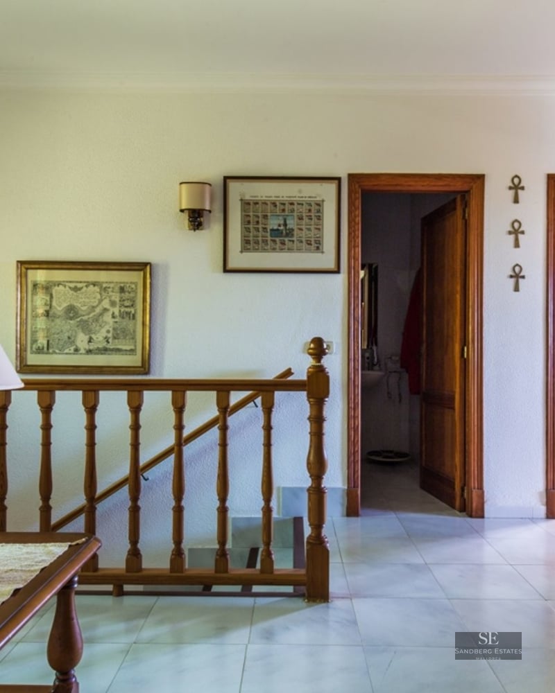 Landing with wooden railing, bookshelf, coffee table, and lamp. White walls and tiled floor.