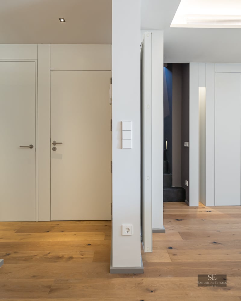 Modern hallway featuring white walls, minimalist doors, and light oak hardwood flooring.