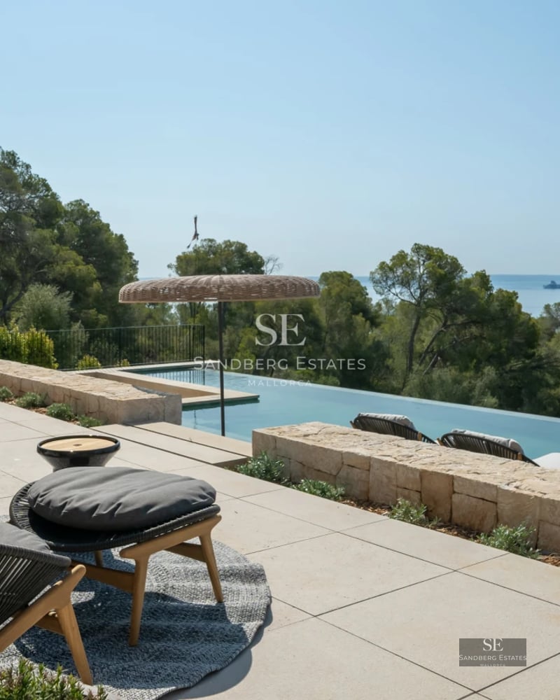 Exterior of a modern villa featuring an infinity pool, large windows, and a terrace with panoramic views. Minimalist design and lush gardens.