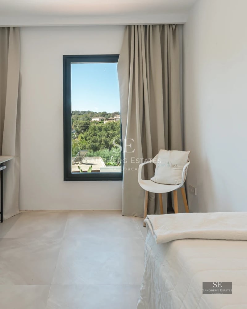 View of an elegant swimming pool surrounded by sun loungers, with a modern villa in the background and lush greenery.
