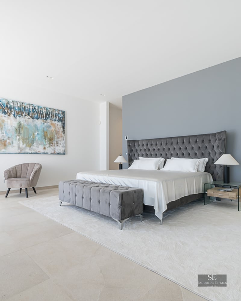 Master bedroom featuring a grey tufted bed, velvet seating area, and a walk-in wardrobe in the background.