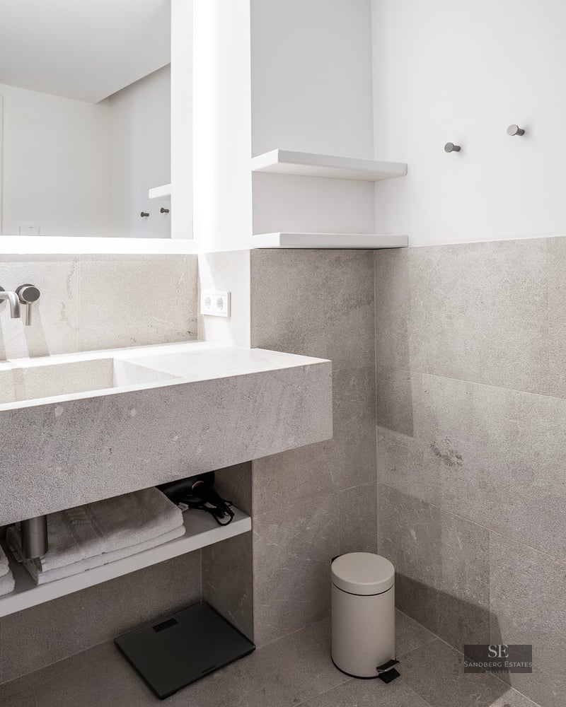 Salle de bain moderne avec vanité flottante en pierre grise, lavabo intégré et grand miroir rétroéclairé.