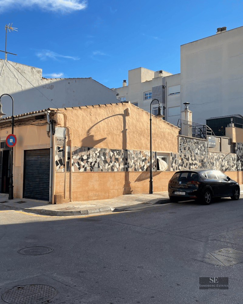 Peach-colored corner building with a mosaic tile strip on a sunny urban street with parked cars and blue sky.