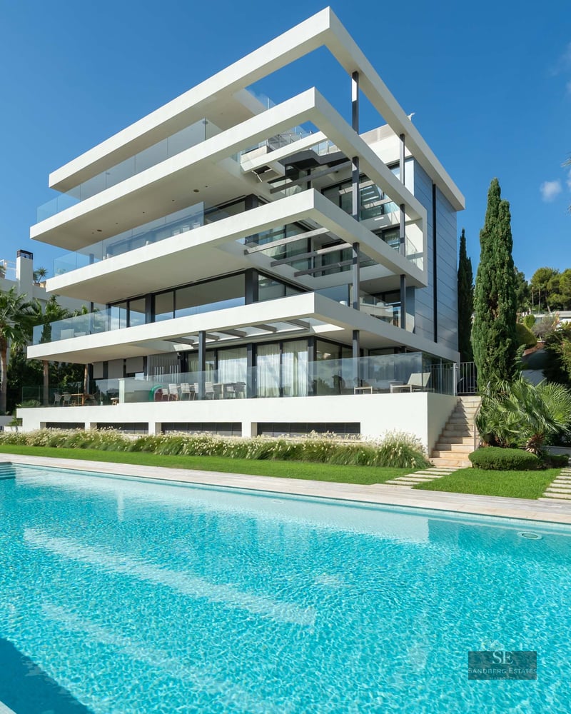 Exterior view of a modern multi-level villa featuring a large turquoise swimming pool and landscaped garden.