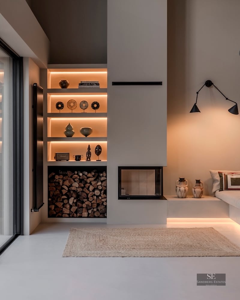 Salon minimaliste moderne avec canapé intégré, éclairage encastré, cheminée et grandes baies vitrées coulissantes.