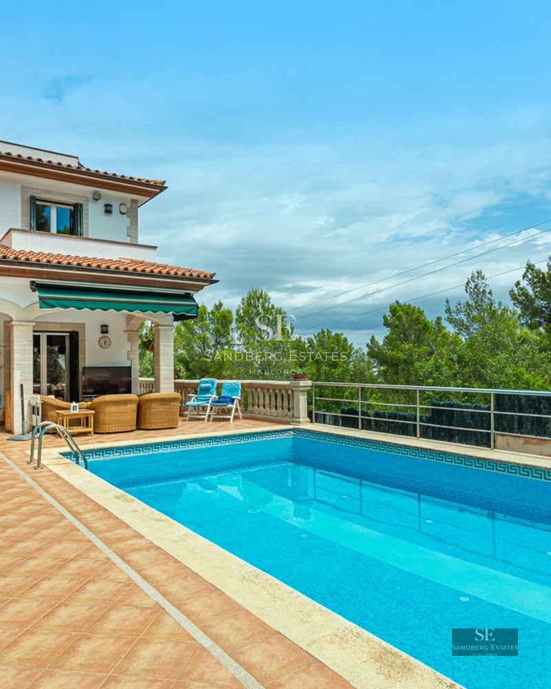 Exterior of modern villa with pool. Large glass windows reflect light. Manicured garden with green lawn and lush vegetation.