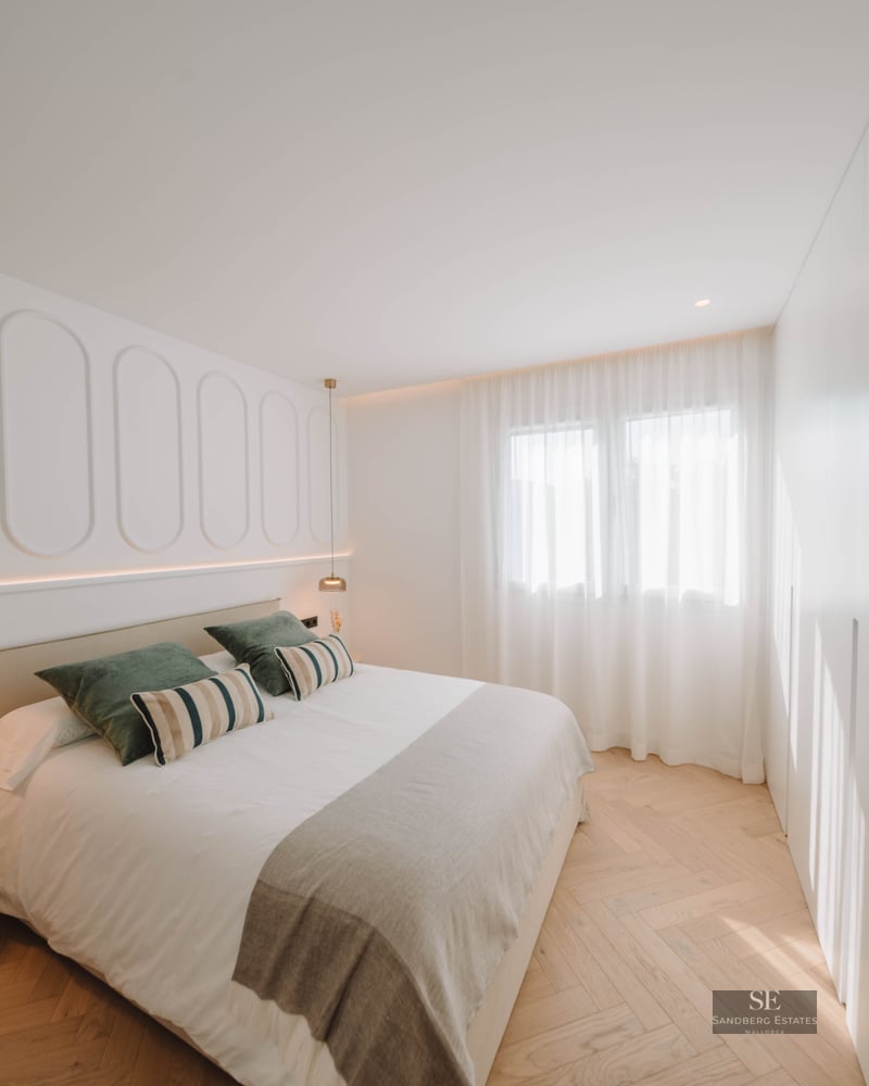 Modern master bedroom featuring a double bed, decorative wall molding, and light wood herringbone floors.