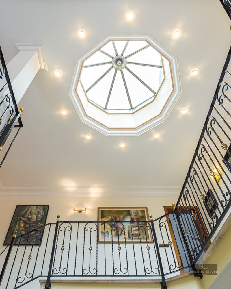 Upward view of a grand staircase with wrought iron railings and a large octagonal skylight in the ceiling.