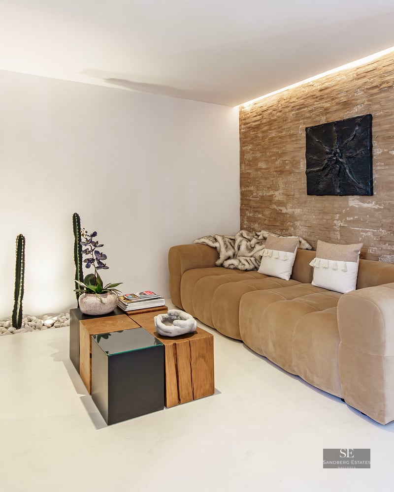 Modern lounge featuring a tan sofa, rustic stone accent wall, large turquoise vase, and indoor cactus garden.