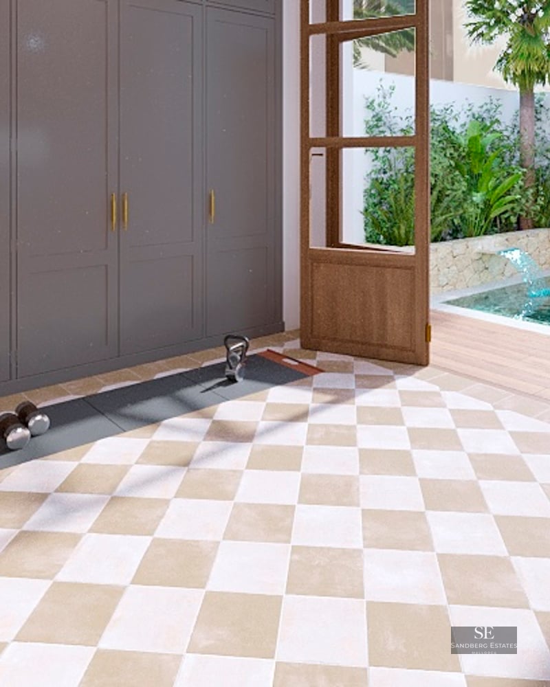 Indoor home gym with weights and bench, open to a tropical courtyard with a small pool and stone wall.