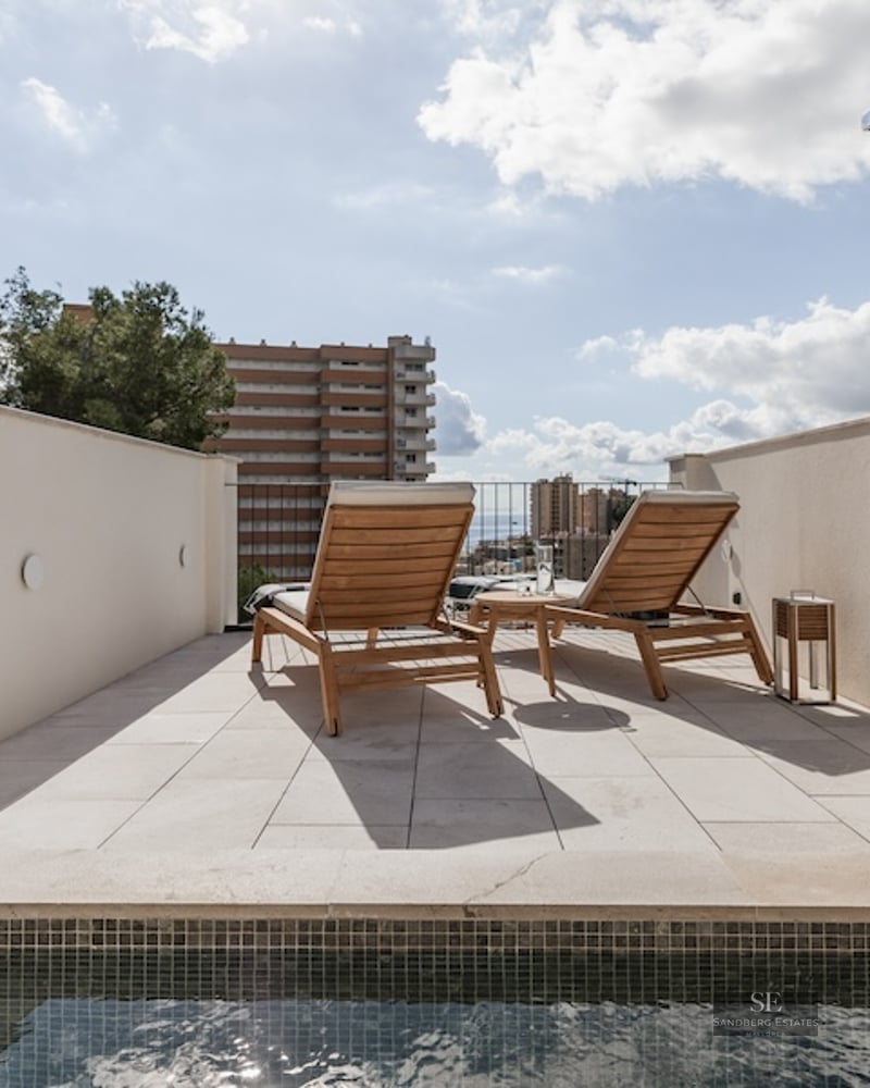 Sunny terrace featuring a small pool, two wooden loungers, and an outdoor shower under a bright blue sky.