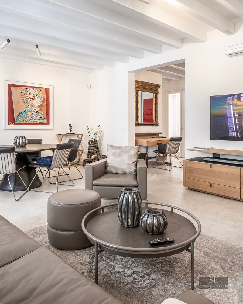 Spacious modern living room with grey leather sofas, wooden ceiling beams, large TV, and adjacent dining area with art.
