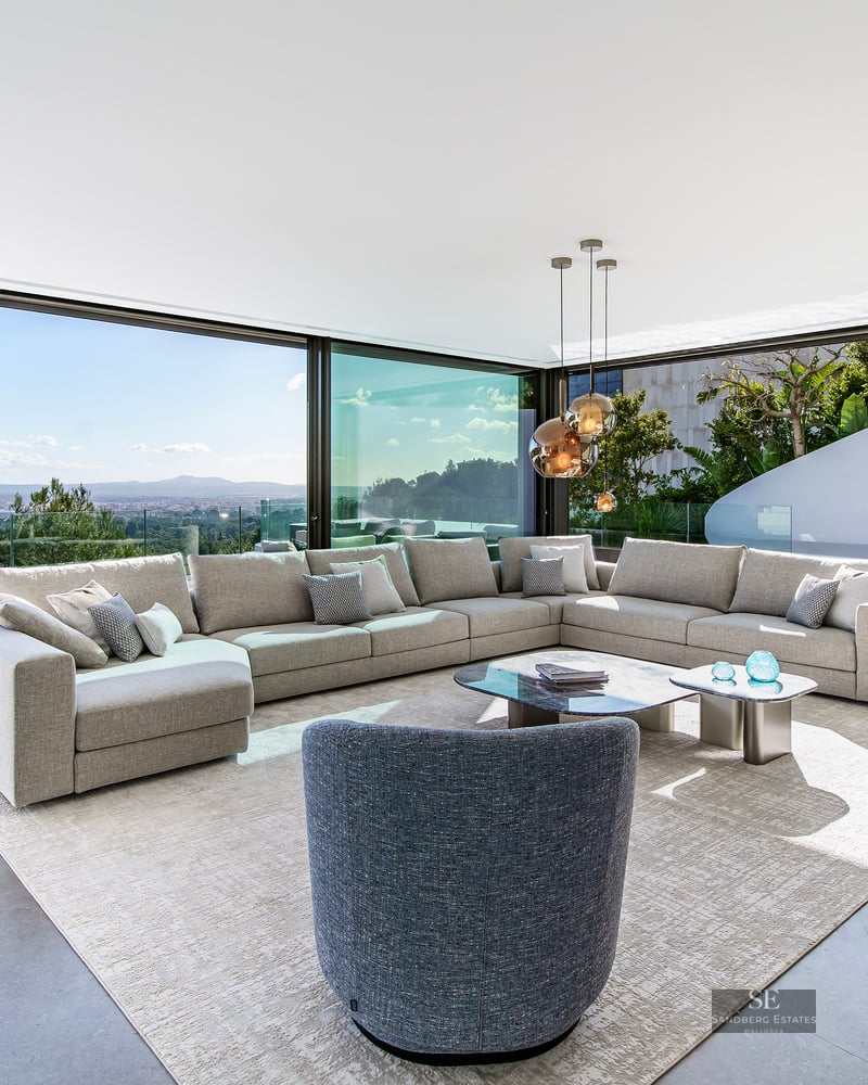 Modern bright living room with large grey sectional sofa and floor-to-ceiling windows overlooking a scenic valley.