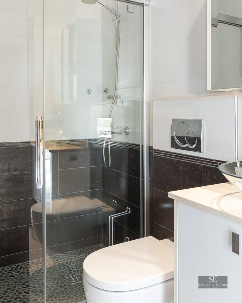 Modern bathroom featuring a glass bowl sink, white vanity, and a glass-enclosed shower with pebble tile floor.