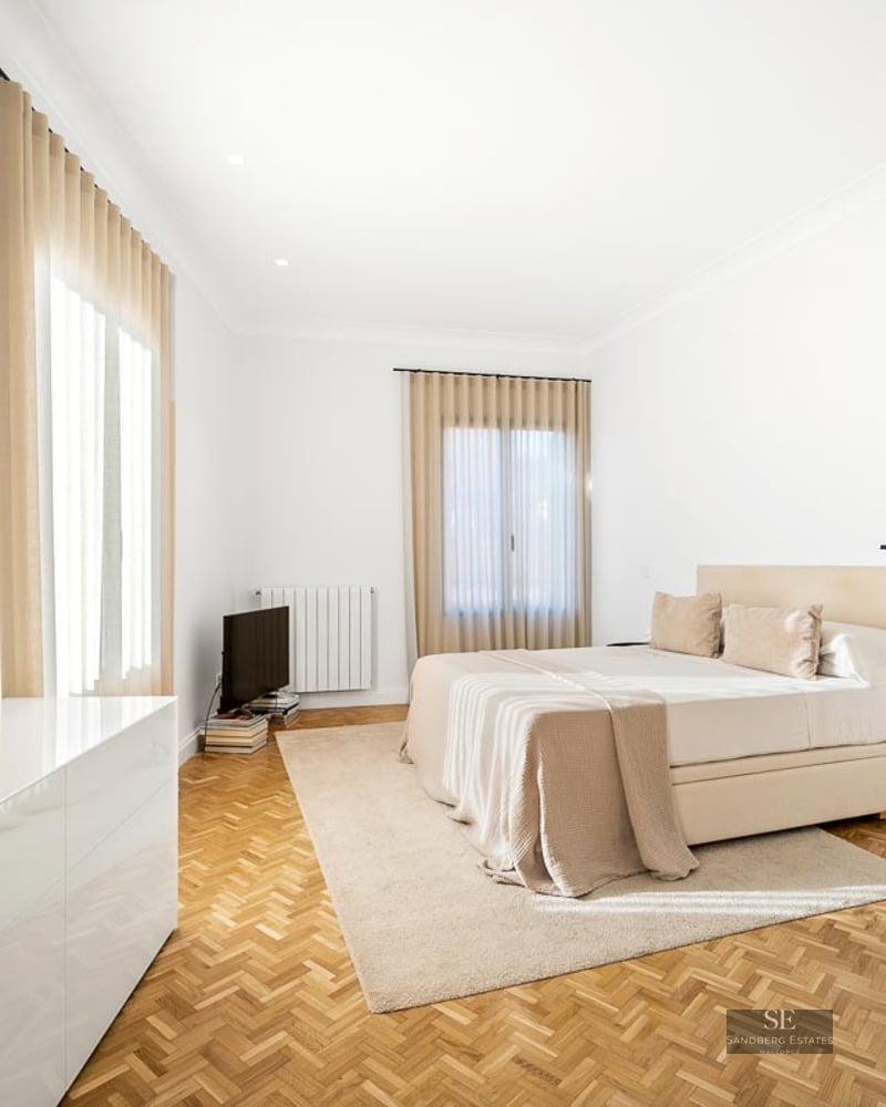 Bright bedroom with herringbone wood floor, large bed, beige curtains, and minimalist designer floor lamp.