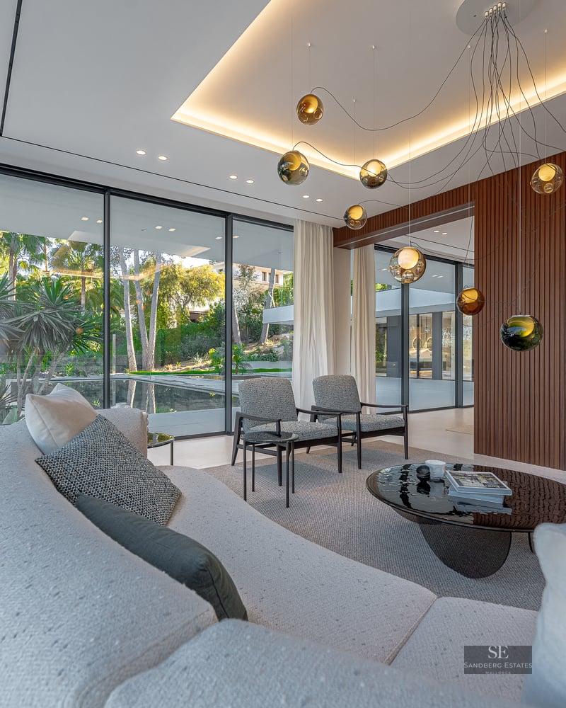 A contemporary living room featuring a curved sofa, designer lighting, and large windows overlooking a lush garden.