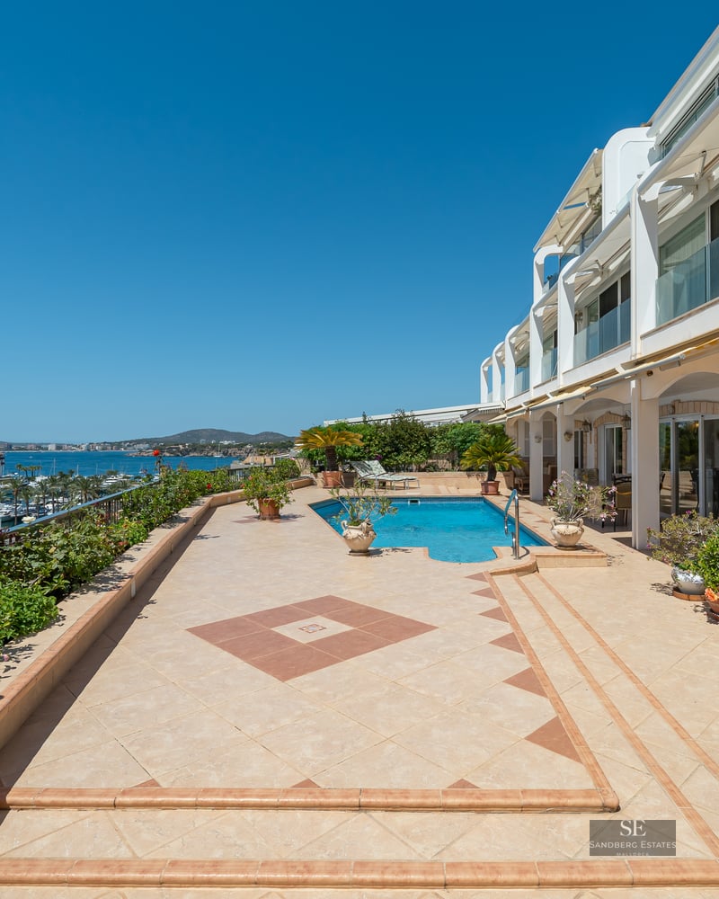 Expansive outdoor terrace with a swimming pool overlooking a marina with yachts under a clear blue sky.