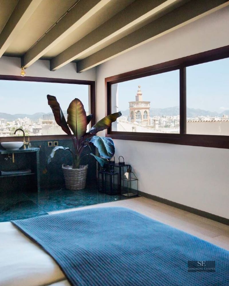Modern bedroom with exposed wood beams, panoramic windows showing a city skyline and cathedral.