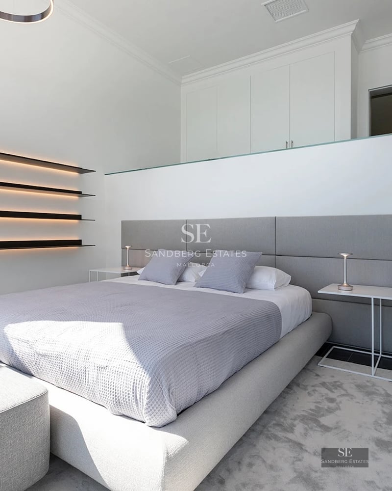 Modern bedroom featuring a grey upholstered bed, backlit wall shelves, and black stairs leading to an upper level.