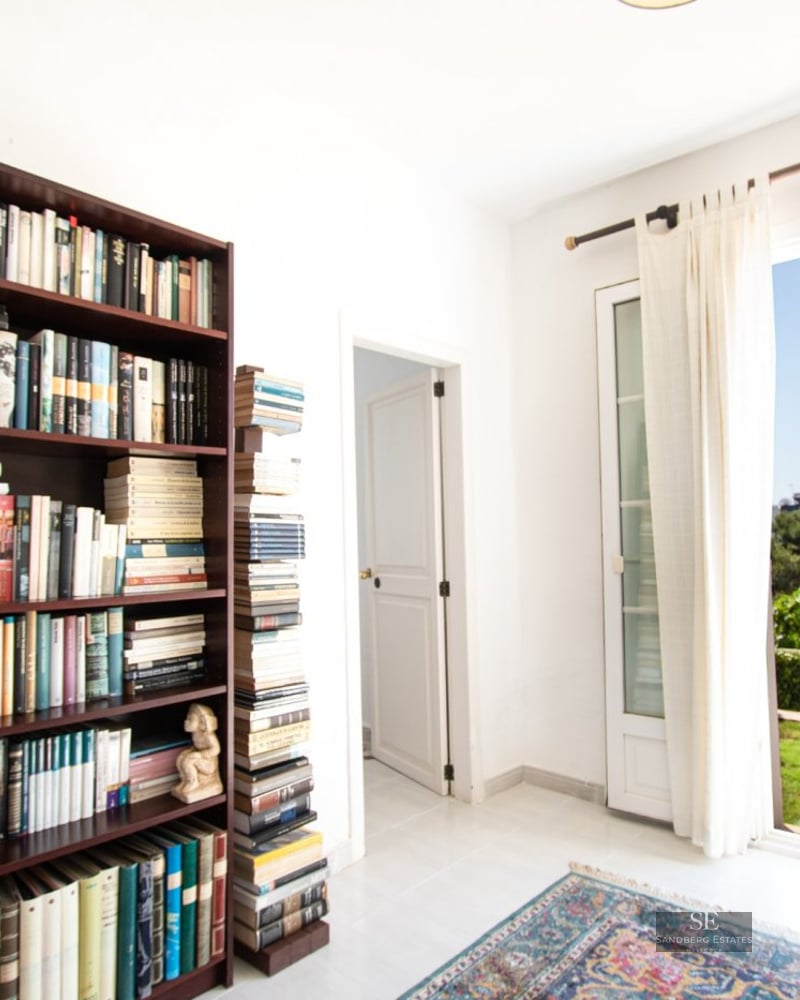 A room featuring a large dark wood bookshelf filled with books and an open door leading to an outdoor swimming pool.
