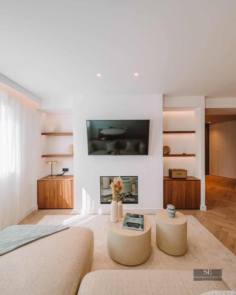 Bright living room featuring a wall-mounted TV, electric fireplace, herringbone wood floors, and cream sofas.
