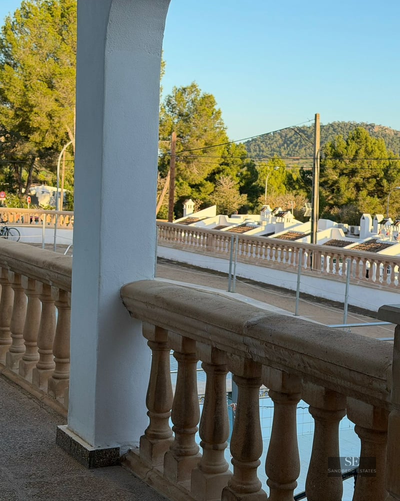 View from a stone balustrade balcony overlooking a Mediterranean neighborhood with white houses and green hills.