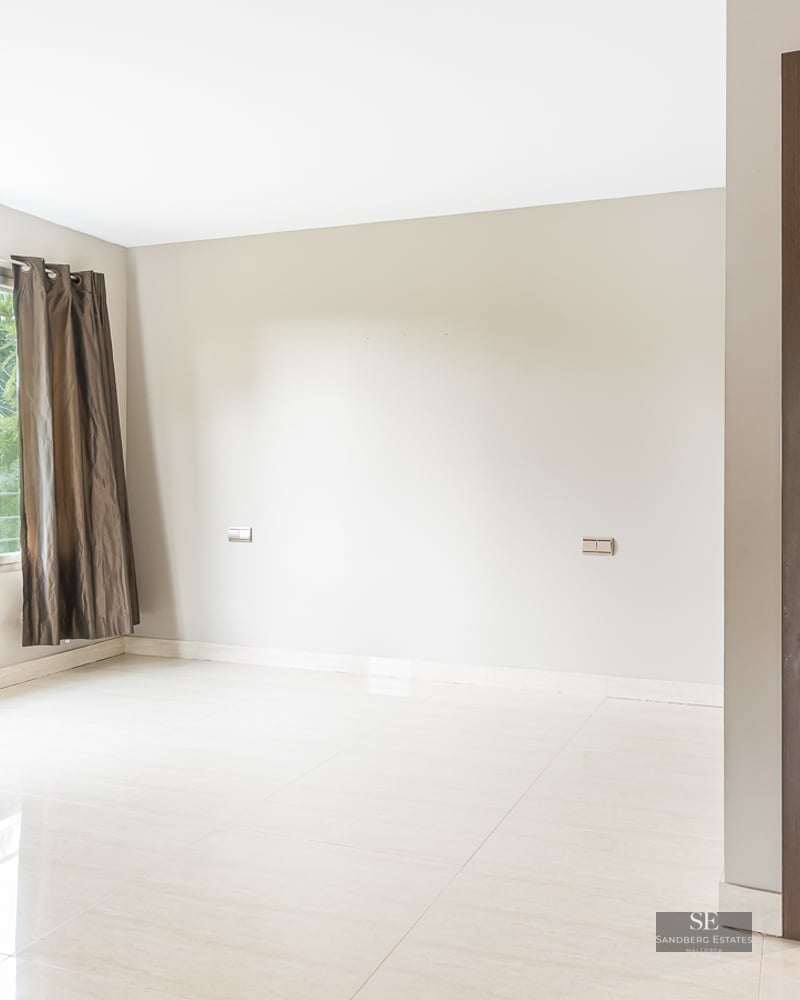 Empty modern bedroom with polished cream tile floors, a window with dark curtains, and an open doorway to an ensuite bathroom.