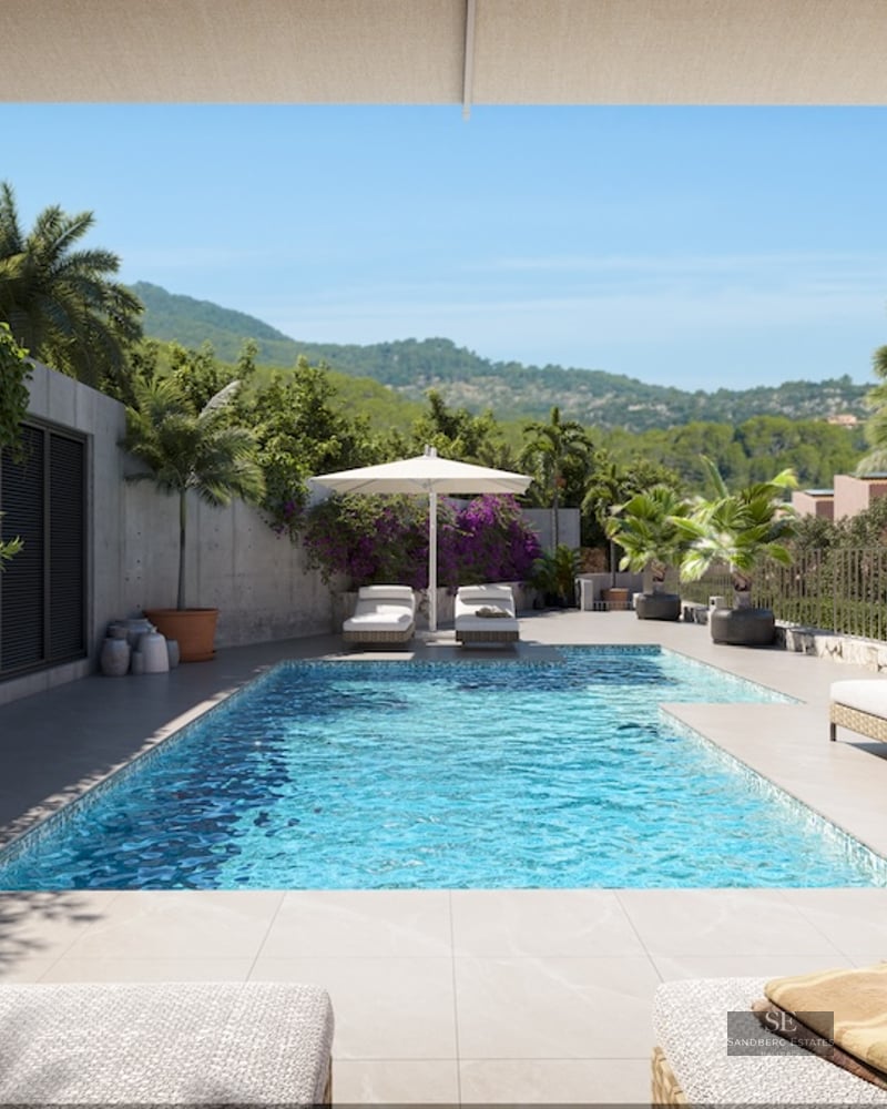 Sun-drenched pool area with white loungers, potted palm trees, and a view of lush green hills under a blue sky.