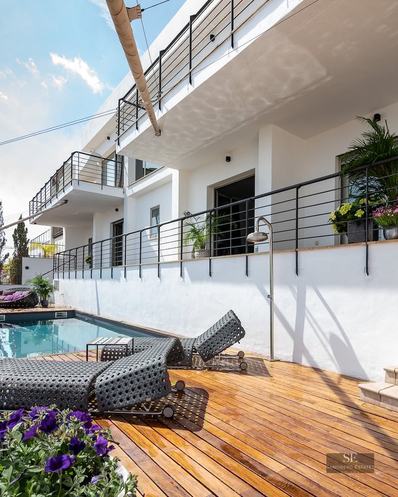 A modern swimming pool area with a wooden deck, loungers, and white architectural facade with black railings.
