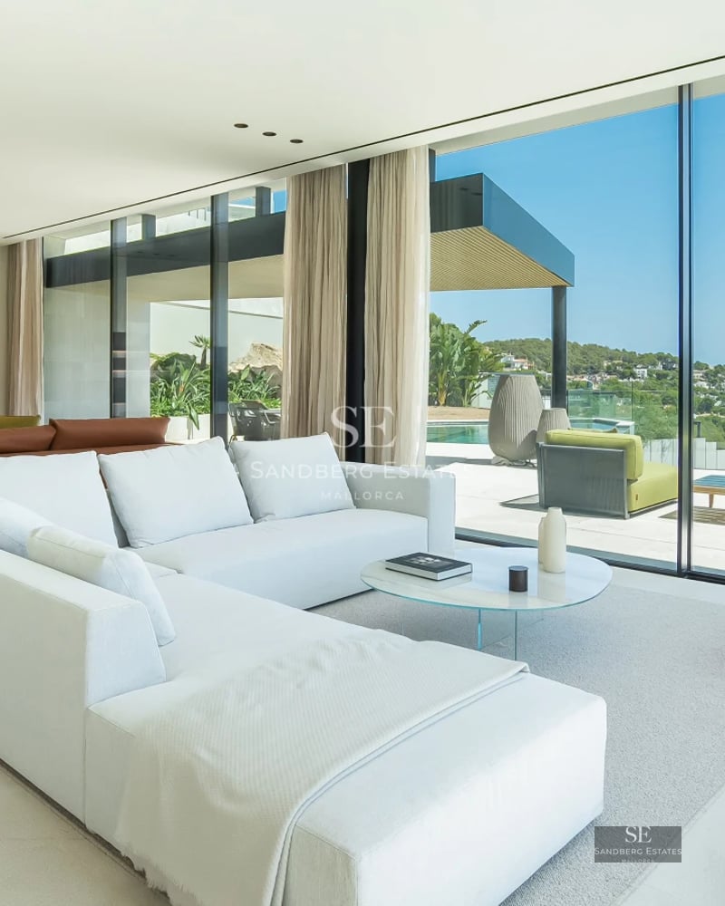 View of a luxury villa with a pool, featuring large windows and a modern design. Lush garden and blue sky.