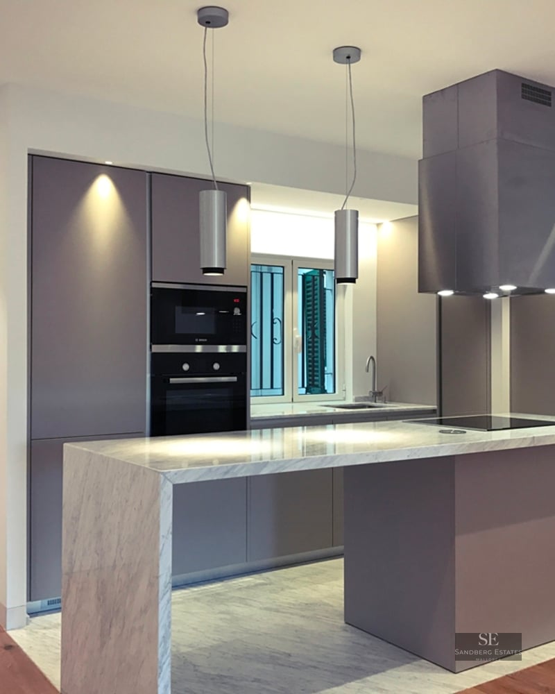 Modern kitchen featuring a purple island with a marble countertop, sleek cabinets, and designer pendant lighting.