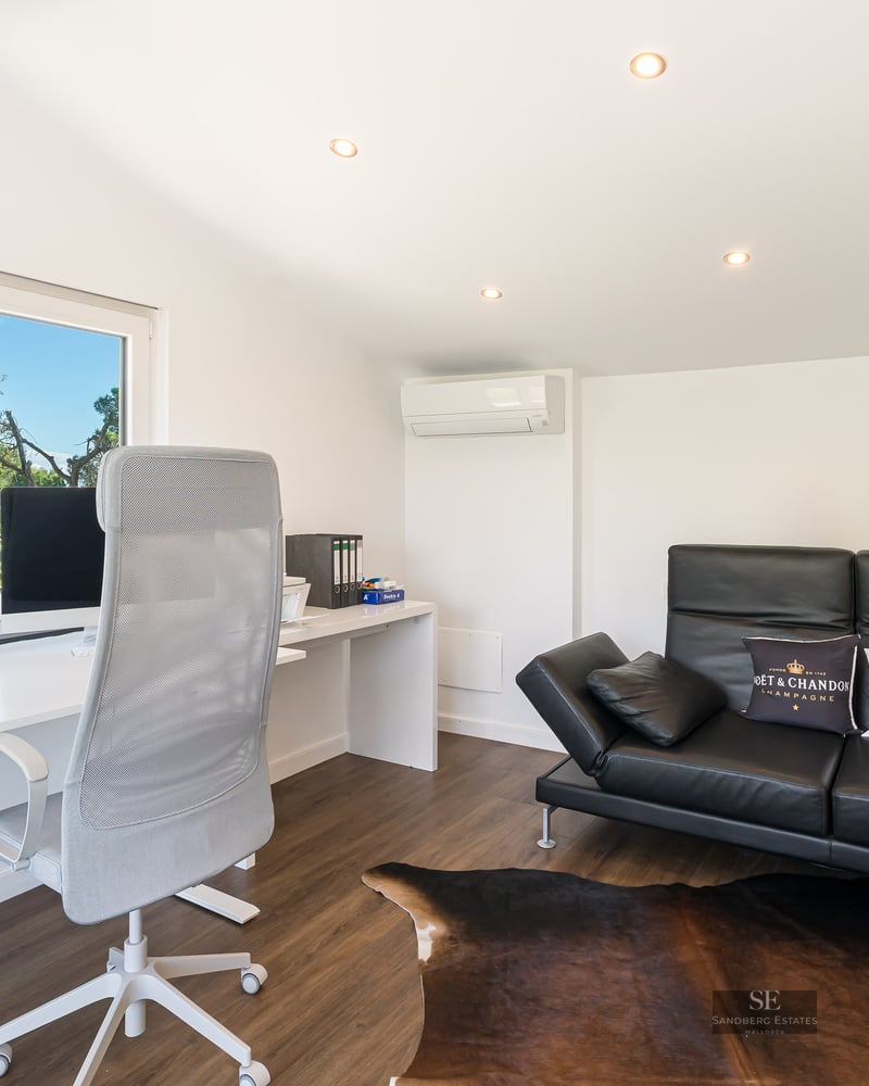Bureau lumineux avec table blanche, chaise ergonomique et canapé en cuir noir devant une fenêtre donnant sur la mer.