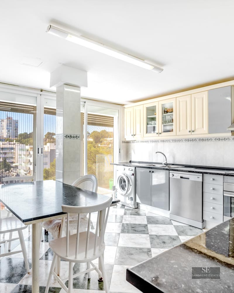 Bright kitchen with checkered marble floor, granite dining table, white chairs, and large windows overlooking the city.