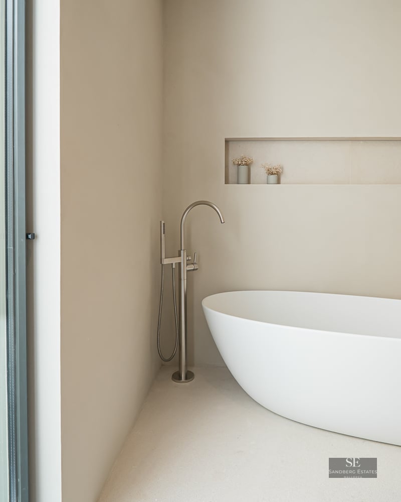 Minimalist bathroom featuring a white freestanding bathtub next to a floor-to-ceiling window with a garden view.