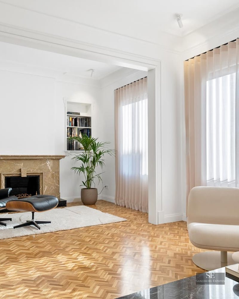 Bright living room with herringbone floors, a marble fireplace, and an Eames chair.