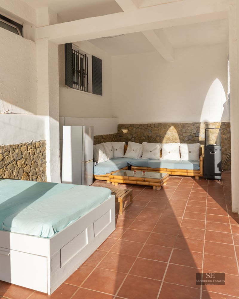 Terrasse couverte avec sols en terre cuite, lit de jour extérieur, banquette, murs en pierre et escalier carrelé.