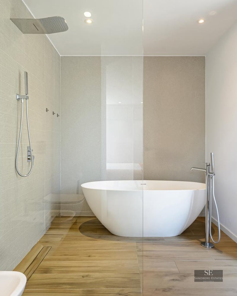 Modern bathroom featuring a freestanding white bathtub, a glass walk-in shower, and wood-look flooring.