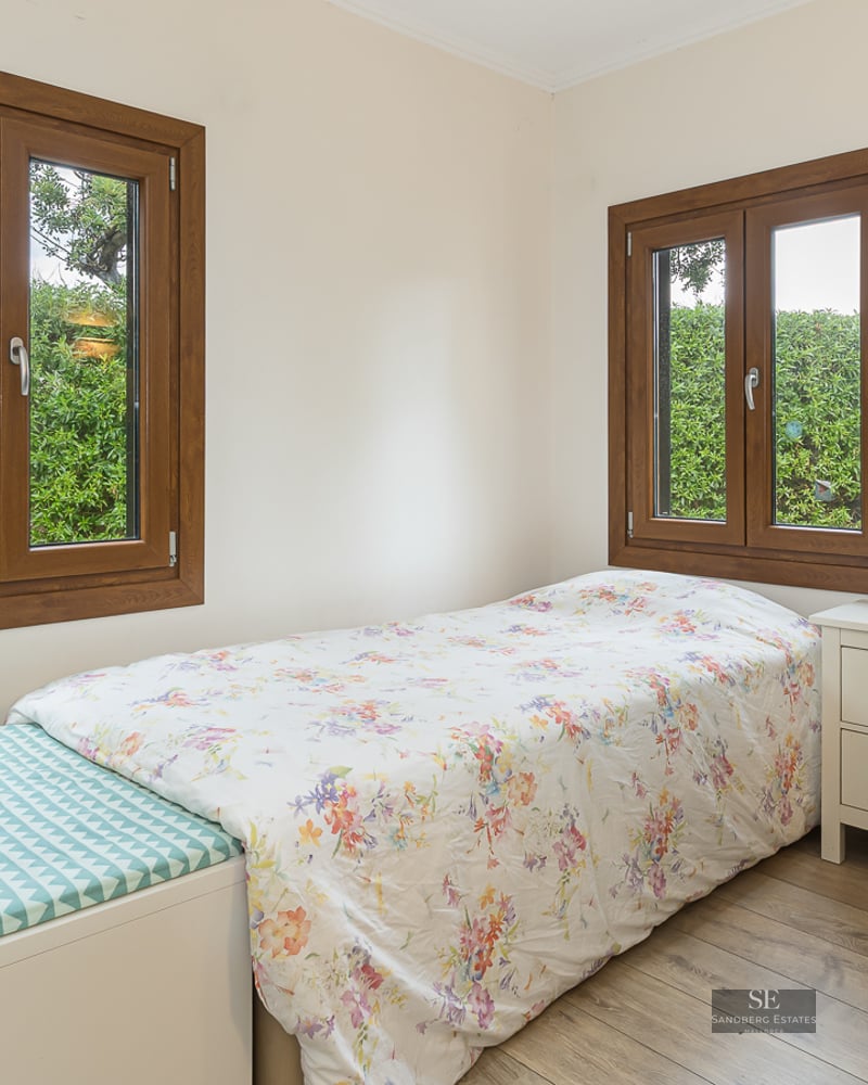 Bright bedroom with a single bed, desk, office chair, and wooden windows overlooking a green garden.