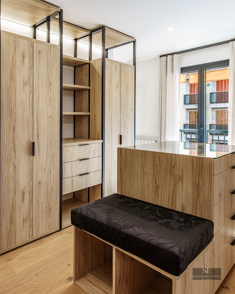 Grand dressing avec armoires en bois clair, îlot central avec plateau en verre et banc noir.